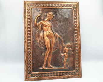 May include: A rectangular copper relief sculpture featuring a classical female figure holding a fan, and a small cherub. The figures are in a detailed, three-dimensional style, set against a textured background, framed with a decorative border.