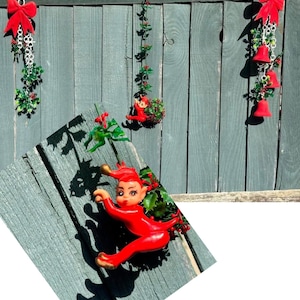 May include: Three hanging festive decorations featuring red velvet bows, green holly leaves, red berries, and small red bells. One decoration includes a small red elf figurine with gold-tipped shoes and hat, suspended by a thin green wire stem.