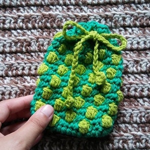 May include: A small green and lime green crocheted pouch with a drawstring closure. The pouch is made with a textured stitch that creates a polka dot pattern.