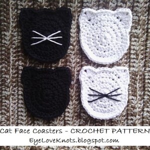 May include: Four crocheted cat face coasters, two black and two white. The coasters are made with a simple stitch pattern and have black yarn whiskers.