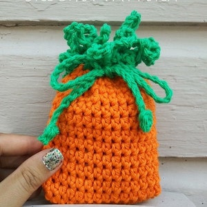 May include: A crocheted carrot-shaped soap cozy or small gift bag. The cozy is orange with green crocheted leaves on top. The text "CARROT SOAP COZY (OR SMALL GIFT BAG) CROCHET PATTERN" is at the top of the image.