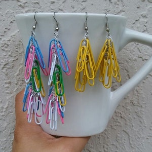 May include: Three pairs of colourful paper clip earrings. The earrings are made with paper clips and crocheted thread. The earrings are hanging from a white mug. The text "THREAD & PAPER CLIP EARRINGS" is at the top of the image. The text "CROCHET PATTERN & JEWELRY DIY EyeLoveKnots" is at the bottom of the image.