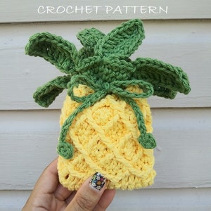 Könnte beinhalten: Gehäkelte Ananas-Seifenhülle oder kleine Geschenktasche. Die Hülle ist gelb mit grünen Blättern und einer grünen Schleife. Der Text "Pineapple Soap Cozy (Or Small Gift Bag) Crochet Pattern" befindet sich oben im Bild. Der Text "EyeLoveKnots" befindet sich unten im Bild.