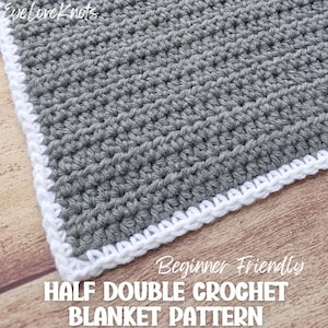 Puede incluir: Primer plano de una manta de ganchillo gris con borde blanco. La manta está hecha con punto media vareta. El texto en la imagen dice "Beginner Friendly HALF DOUBLE CROCHET BLANKET PATTERN". La manta está sobre una superficie de madera.