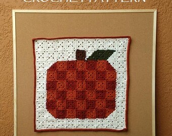 May include: A framed crochet pattern for a pumpkin pixel art project. The pattern is on a corkboard background and features a white crocheted pumpkin with a brown stem and green leaves. The text "Pumpkin Pixel Art CROCHET PATTERN" is at the top of the frame and the text "By EyeLoveKnots" is at the bottom of the frame.
