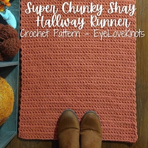 May include: A rust-coloured, chunky crochet hallway runner. The text on the rug reads "Super Chunky Shay Hallway Runner Crochet Pattern - EyeLoveKnots". Brown boots are at the bottom of the rug.