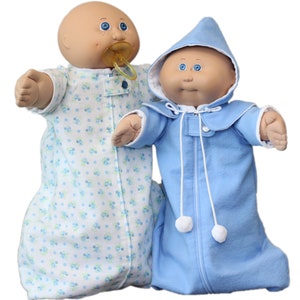 May include: Two Cabbage Patch Kids dolls. One doll wears a light blue and white floral print sleep sack and has a dummy. The other doll is in a light blue hooded sleep sack with white pom-poms and a zip.
