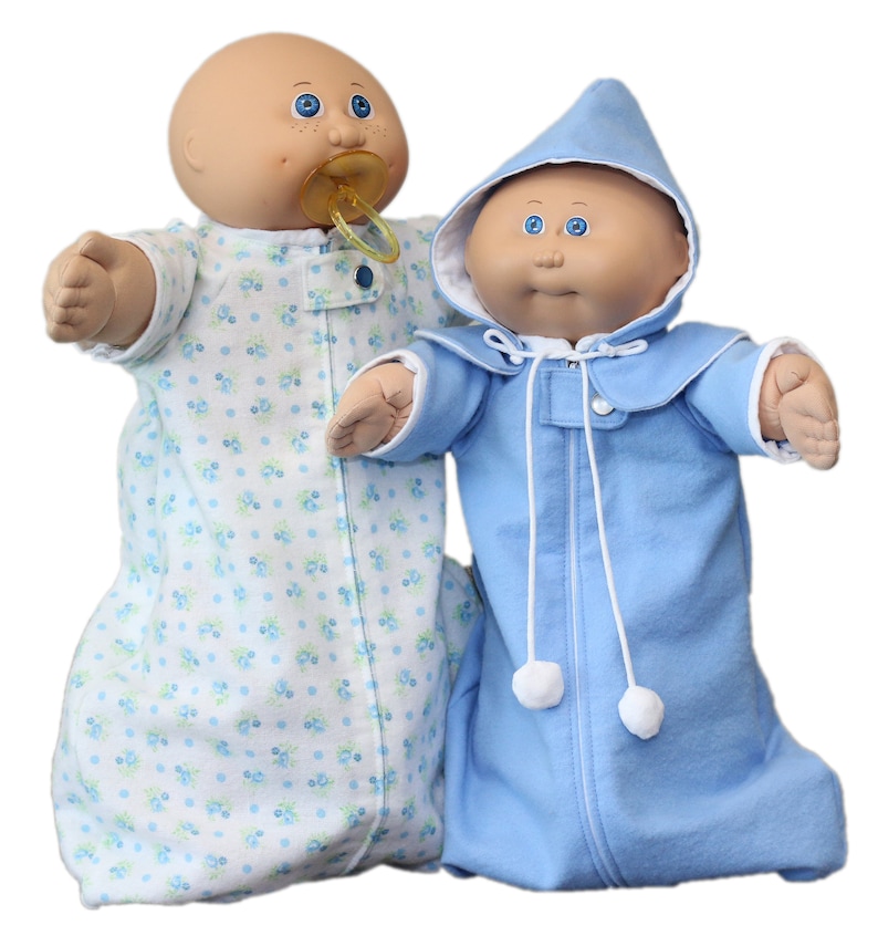 May include: Two Cabbage Patch Kids dolls. One doll wears a light blue and white floral print sleep sack and has a dummy. The other doll is in a light blue hooded sleep sack with white pom-poms and a zip.