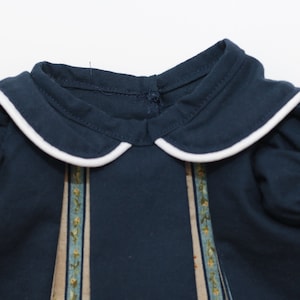May include: Navy blue dress with a white-trimmed Peter Pan collar and short, puffed sleeves. The dress features vertical panels with a floral design in shades of blue, green, and yellow.