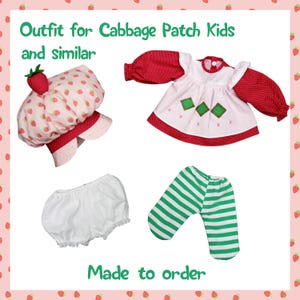 May include: Outfit for Cabbage Patch Kids and similar dolls, including a red and white dress with green accents, a white hat with red strawberries, white bloomers, and green and white striped pants.