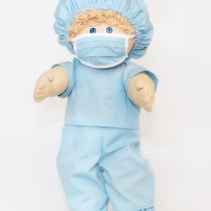 K&ouml;nnte beinhalten: Eine Puppe in hellblauer medizinischer Kleidung, einschlie&szlig;lich einer M&uuml;tze, eines Hemdes, einer Hose und einer Gesichtsmaske. Die Puppe hat blondes Haar, blaue Augen und ist so gestaltet, dass sie einem Angeh&ouml;rigen der Gesundheitsberufe &auml;hnelt. Die Kleidung der Puppe besteht aus einem weichen Stoff.