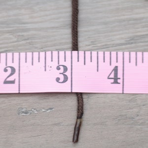 May include: A brown cord or string measured against a pink ruler. The cord is about 3 inches long.