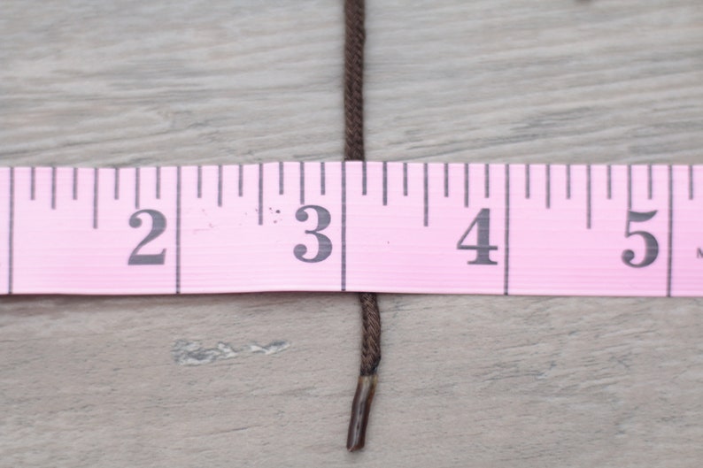 May include: A brown cord or string measured against a pink ruler. The cord is about 3 inches long.