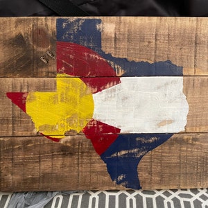 May include: A wooden sign with a distressed paint finish depicting the state of Texas in the colors of the Colorado flag: yellow, red, white, and blue.