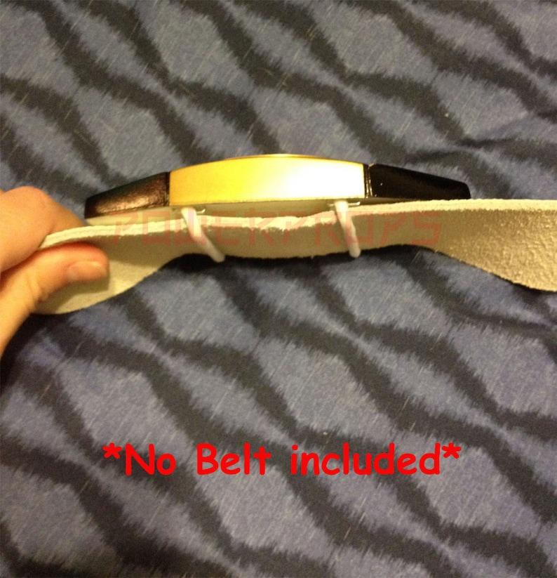 May include: A gold-colored belt buckle with black accents is attached to a light tan leather belt. The text "*No Belt included*" is written in red. The buckle is held together with white elastic.