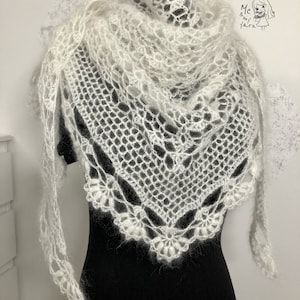 May include: A white, open-weave crochet shawl with a delicate floral border. The shawl is draped over a black form, showcasing its intricate design and soft texture. The image includes the text "Me & my yarn".