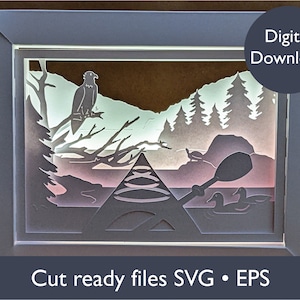May include: A layered paper art piece depicting a serene lake scene with an eagle perched on a branch, a kayak, and ducks. The artwork is framed in a light gray border, with the text "Digital Download" and "Cut ready files SVG • EPS".
