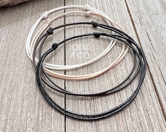 May include: Three different colored cords are layered on top of each other. The cords are white, beige, and black. The cords are tied together at the ends.