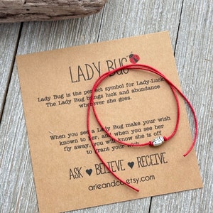May include: Red string bracelet with a silver ladybug charm. The bracelet is tied around a card with the text "Lady Bug is the perfect symbol for Lady-Luck. The Lady Bug brings luck and abundance wherever she goes. When you see a Lady Bug make your wish known to her, and when you see her fly away, you will know she is off to grant your wish. ASK BELIEVE RECEIVE arieandco etsy.com"