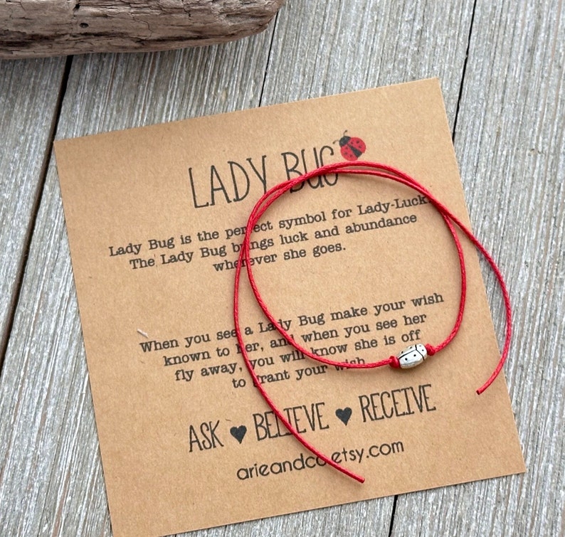 May include: Red string bracelet with a silver ladybug charm. The bracelet is tied around a card with the text "Lady Bug is the perfect symbol for Lady-Luck. The Lady Bug brings luck and abundance wherever she goes. When you see a Lady Bug make your wish known to her, and when you see her fly away, you will know she is off to grant your wish. ASK BELIEVE RECEIVE arieandco etsy.com"