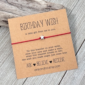 May include: Red string bracelet with a silver star charm on a brown card with the text "Birthday Wish" and "A little gift from me to you."  The card also includes instructions on how to tie the bracelet and make a wish. The text "Ask ♥ Believe ♥ Receive" and the website "arieandco.etsy.com" are also included on the card.