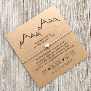 May include: A gray string bracelet with a silver heart charm and a card that reads "Wherever you go, go with all your heart. Tie this bracelet on your wrist, close your eyes and make a wish, when this bracelet breaks in two, the wish you made might just come true. ASK BELIEVE RECEIVE arieandco.etsy.com"