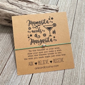 May include: A green string bracelet with a silver star charm. The card attached to the bracelet reads "Mamasita needs a Margarita" with a margarita glass graphic. The card also includes instructions for making a wish and the text "Ask Believe Receive".