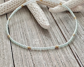 May include: A delicate, light blue beaded necklace with gold accents. The necklace is made of small, round beads and is strung on a thin, gold chain.