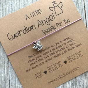 May include: A purple string bracelet with a silver angel charm. The card attached to the bracelet reads "A Little Guardian Angel Specially for You" and includes the text "Tie this bracelet on your wrist, close your eyes and make a wish, when this bracelet breaks in two, the wish you made might just come true. ASK BELIEVE RECEIVE arieandco.etsy.com".