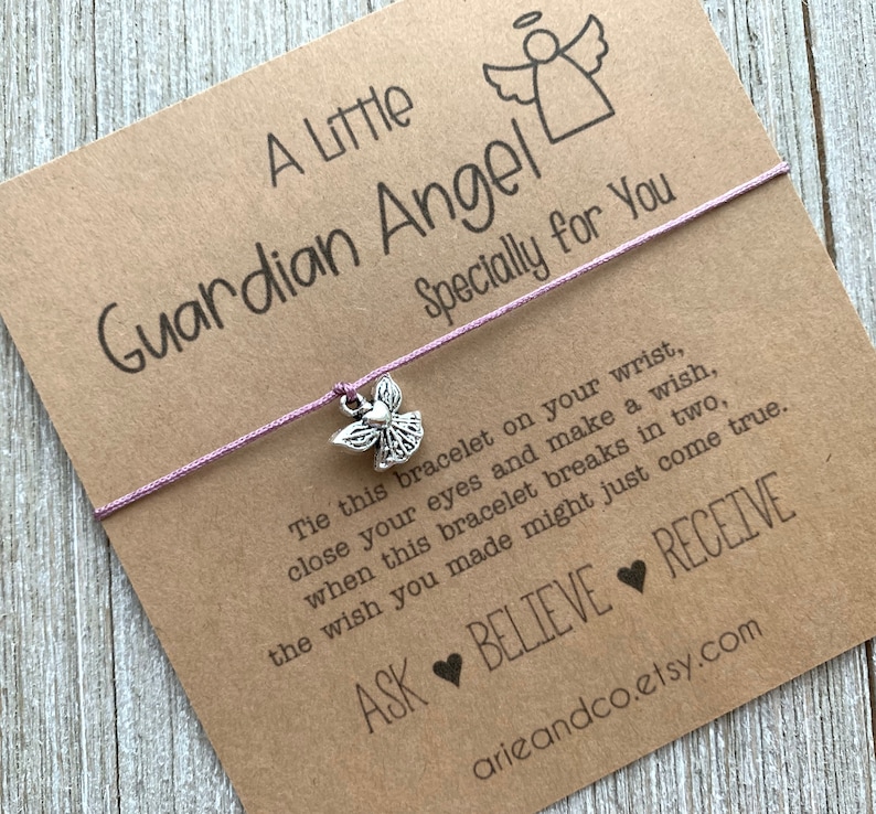 May include: A purple string bracelet with a silver angel charm. The card attached to the bracelet reads "A Little Guardian Angel Specially for You" and includes the text "Tie this bracelet on your wrist, close your eyes and make a wish, when this bracelet breaks in two, the wish you made might just come true. ASK BELIEVE RECEIVE arieandco.etsy.com".