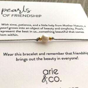 May include: A gray string bracelet with a white pearl and gold beads. The card reads "pearls of friendship" and includes a quote about the beauty of friendship. The card is signed "arie & co."