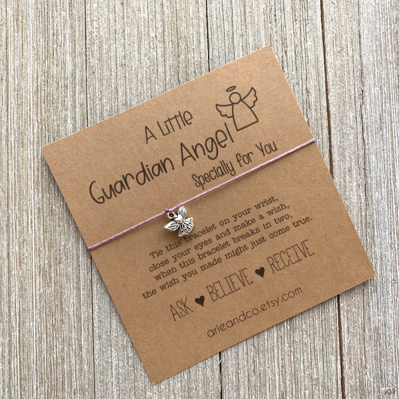 May include: A brown card with the text "A Little Guardian Angel Specially for You" and a pink string bracelet with a silver angel charm. The card also includes the text "Tie this bracelet on your wrist, close your eyes and make a wish, when this bracelet breaks in two, the wish you made might just come true. ASK BELIEVE RECEIVE arieandco.etsy.com"