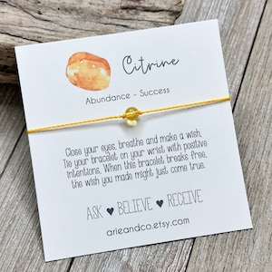 May include: A yellow string bracelet with a small citrine stone bead. The card reads "Citrine, Abundance - Success. Close your eyes, breathe and make a wish. Tie your bracelet on your wrist with positive intentions. When this bracelet breaks free, the wish you made might just come true. ASK BELIEVE RECEIVE arieandco.etsy.com"