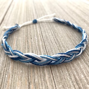 May include: A braided bracelet with white and blue threads. The bracelet is made with a simple knot closure.