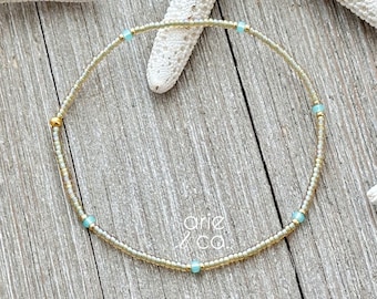 May include: A delicate gold and light blue beaded bracelet with a subtle shimmer. The bracelet is made with tiny beads and features a simple design.