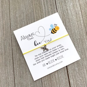 May include: A yellow string bracelet with a silver bee charm. The card attached to the bracelet reads "Always bee You!" and includes instructions on how to make a wish. The card also includes the text "Ask Believe Receive" and the website address arieandco.etsy.com.