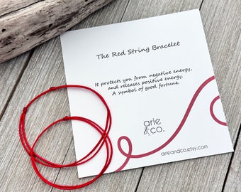 May include: Red string bracelet with a white card that reads "The Red String Bracelet" and "It protects you from negative energy, and releases positive energy. A symbol of good fortune." The card also has the text "arie &Co." and "arieandco.etsy.com".