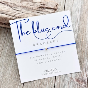 May include: A blue string bracelet with a gold bead. The card reads "The blue cord bracelet" and "Is a powerful symbol of peace, trust, and strength." The card also includes the text "arie & co. arieandco.etsy.com".