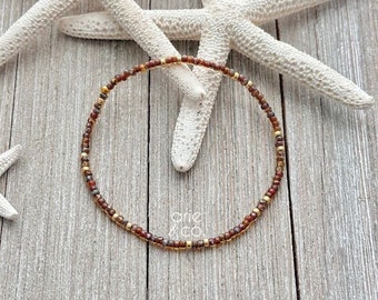 May include: A delicate brown and gold beaded bracelet with a simple design. The bracelet is made with small, round beads and is perfect for layering with other bracelets.