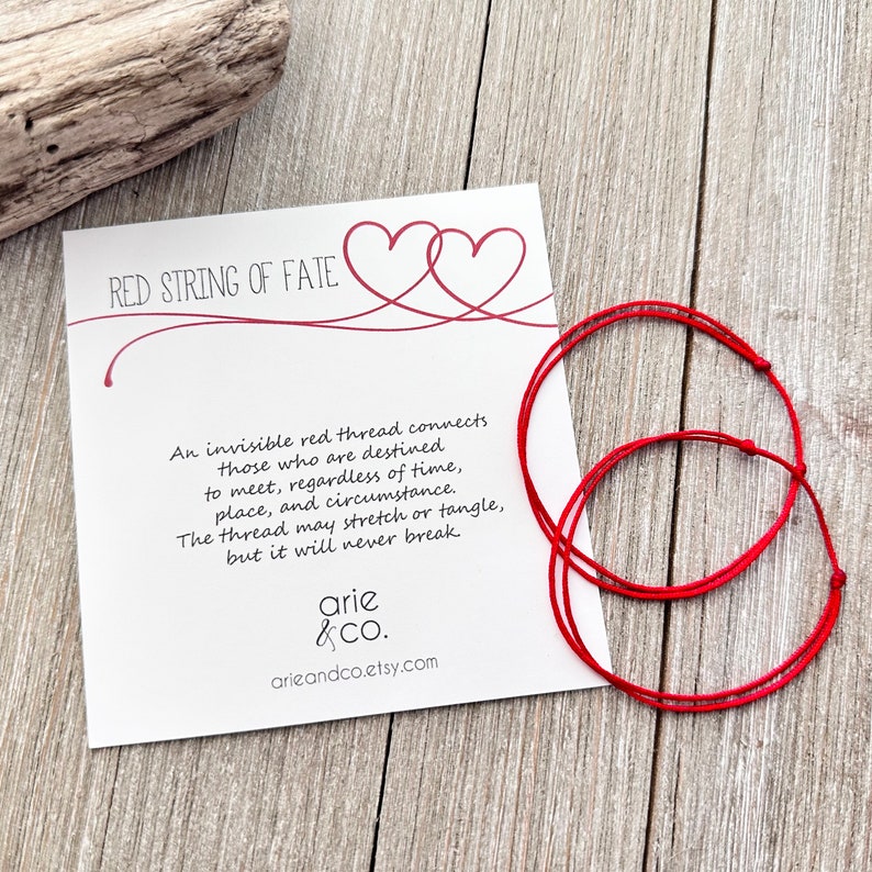 May include: Two red string bracelets with a card that reads "Red String of Fate" and a quote about an invisible red thread connecting those destined to meet. The card also includes the text "arie & co. arieandco.etsy.com"