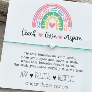 May include: A white card with a rainbow made of colourful paper clips and the words "teach love inspire" in black script. The card also includes the text "Tie this bracelet on your wrist, close your eyes and make a wish, when this bracelet breaks in two, the wish you made might just come true. ASK BELIEVE RECEIVE arieandco.etsy.com".