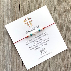 May include: Red string bracelet with a white cross charm and turquoise and white beads. The bracelet comes with a card that reads "THE CROSS" and a message about faith.