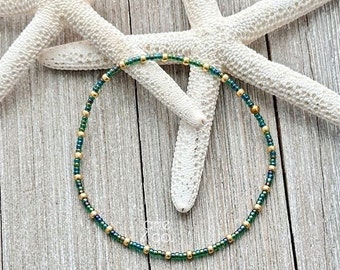 May include: A delicate green and gold beaded bracelet. The bracelet is made with small, round beads that are strung together on a thin wire. The beads are a mix of green and gold, and the bracelet has a simple, elegant design.