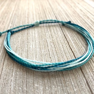 May include: A blue and white ombre friendship bracelet made of braided string.