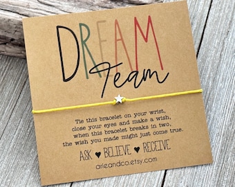 Può includere: Braccialetto di corda giallo con un ciondolo a forma di stella d'argento e un biglietto che recita "Dream Team" in lettere colorate. Il biglietto include anche il testo "Lega questo braccialetto al tuo polso, chiudi gli occhi e fai un desiderio, quando questo braccialetto si romperà in due, il desiderio che hai fatto potrebbe avverarsi. Chiedi ♥ Credi ♥ Ricevi arieandco.etsy.com"