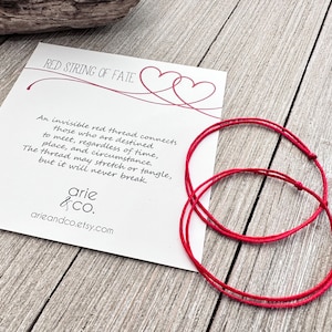 May include: Two red string bracelets with a white card that reads "Red String of Fate" and a quote about an invisible red thread connecting those destined to meet. The card also includes the text "arie &CO. arieandco.etsy.com"