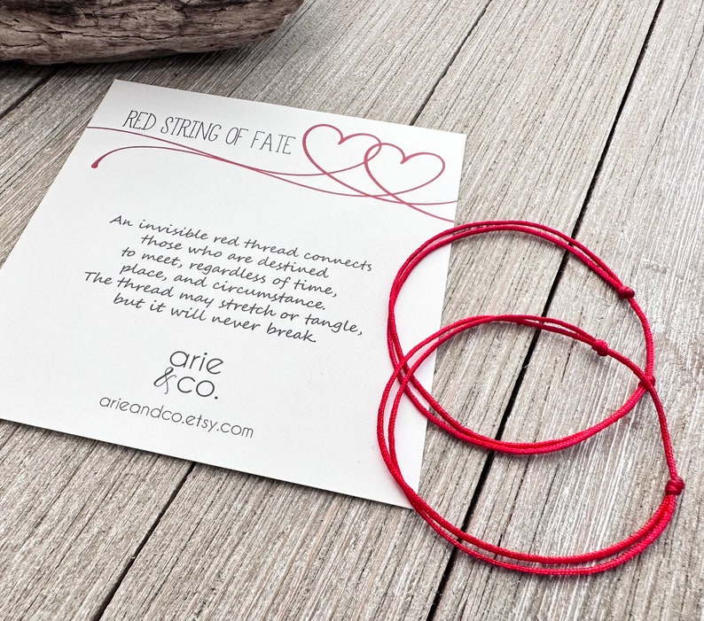 May include: Two red string bracelets with a white card that reads "Red String of Fate" and a quote about an invisible red thread connecting those destined to meet. The card also includes the text "arie &CO. arieandco.etsy.com"