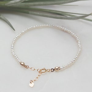 May include: A dainty pearl bracelet featuring a gold heart charm and a gold clasp. The bracelet is made of small, white pearls and is ideal for everyday wear.