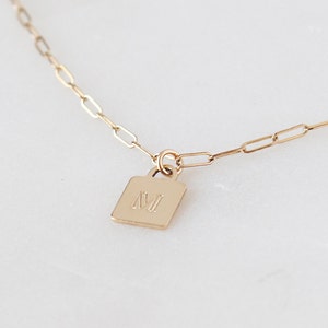 May include: A gold chain necklace with a small square pendant engraved with the letter "M".
