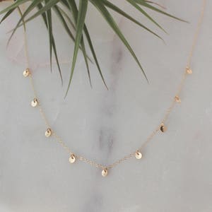 May include: A delicate gold necklace with small, round charms hanging from the chain. The necklace is on a white background.